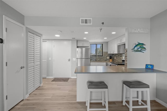 kitchen featuring a breakfast bar, stainless steel refrigerator, white cabinetry, range, and kitchen peninsula