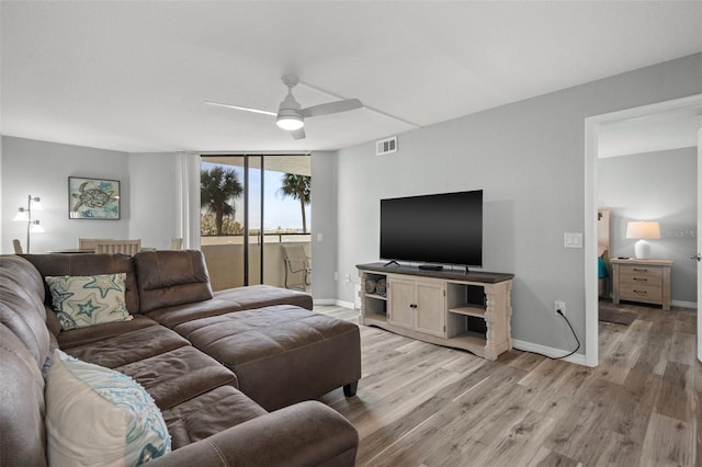 living room with ceiling fan, light hardwood / wood-style floors, and a wall of windows