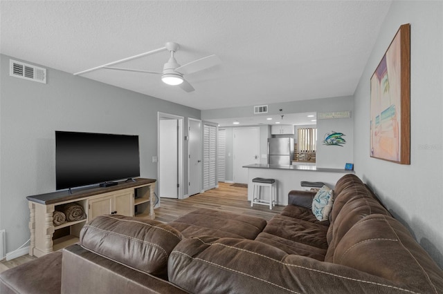 living room featuring ceiling fan, light hardwood / wood-style flooring, and a textured ceiling