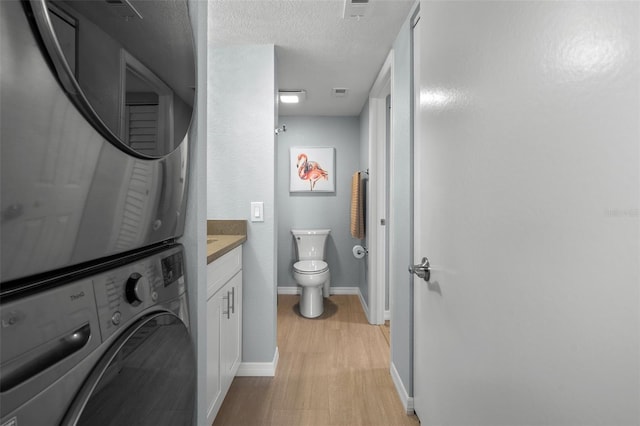 laundry room featuring light hardwood / wood-style flooring, a textured ceiling, and stacked washer / dryer