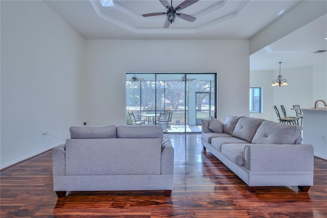 living room with a towering ceiling, dark wood-type flooring, ceiling fan with notable chandelier, and a tray ceiling