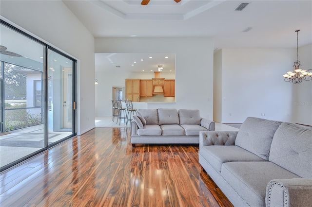 living room featuring dark hardwood / wood-style flooring, ceiling fan with notable chandelier, and a raised ceiling