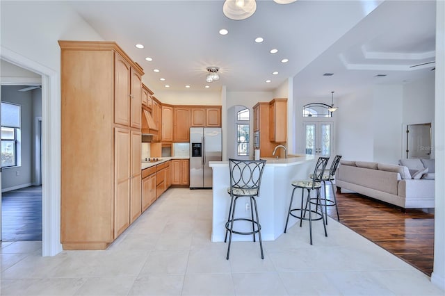 kitchen featuring light brown cabinetry, stainless steel fridge with ice dispenser, a kitchen breakfast bar, kitchen peninsula, and a wealth of natural light