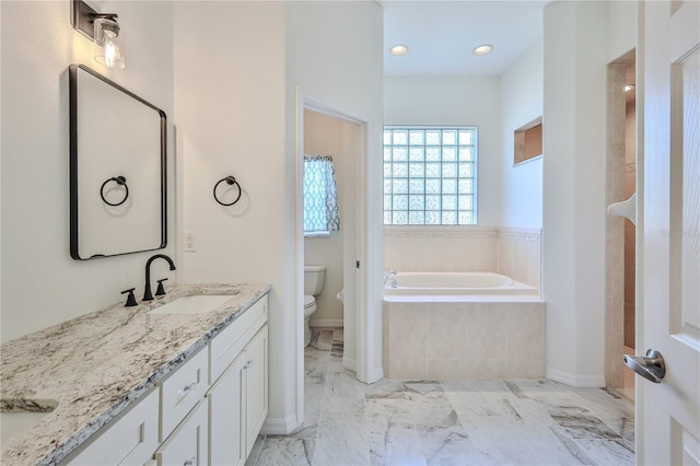 bathroom with tiled tub, vanity, and toilet