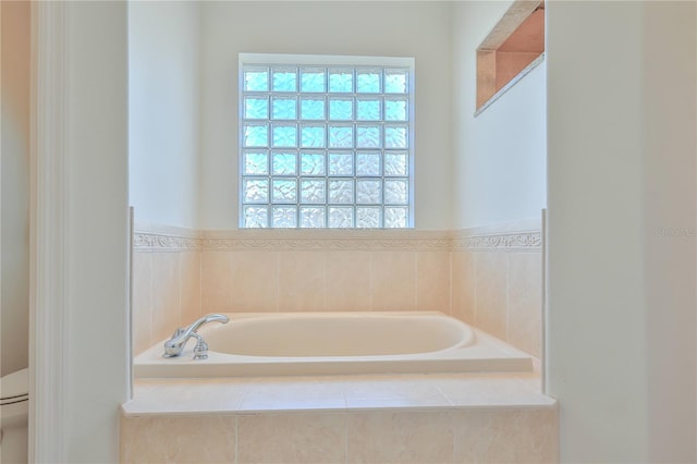 bathroom featuring tiled tub, a wealth of natural light, and toilet