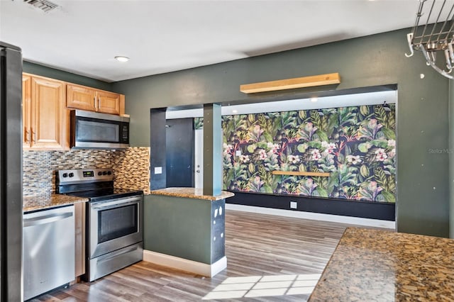 kitchen with tasteful backsplash, stainless steel appliances, light brown cabinetry, and light hardwood / wood-style flooring