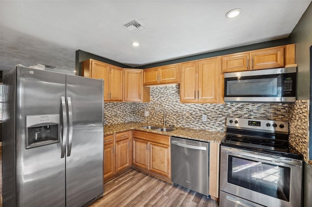 kitchen with visible vents, light stone counters, stainless steel appliances, light wood-type flooring, and a sink