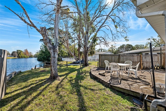 view of yard featuring outdoor dining space, a deck with water view, and a fenced backyard