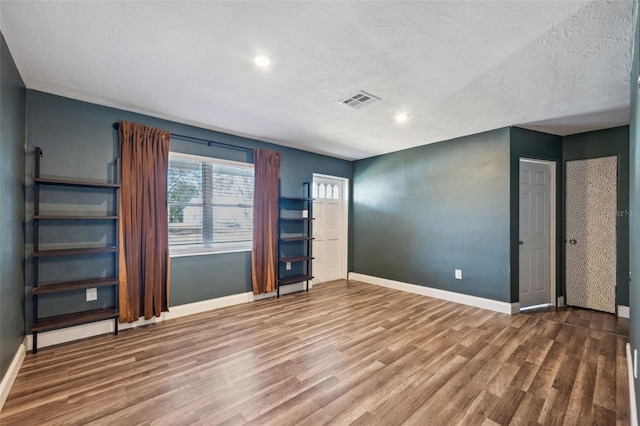 unfurnished room with a textured ceiling, wood finished floors, visible vents, and baseboards