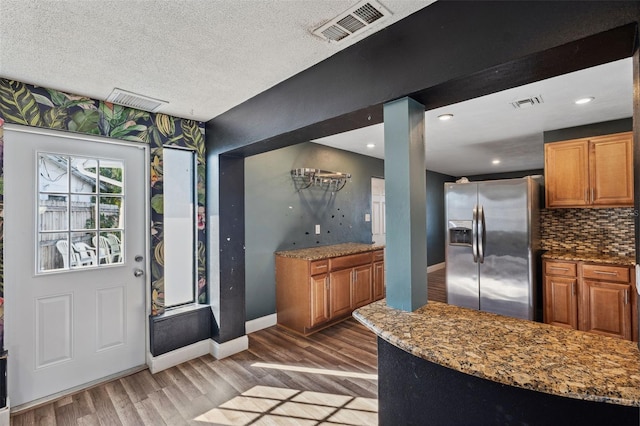 kitchen featuring light wood-style flooring, visible vents, stainless steel refrigerator with ice dispenser, and light stone counters