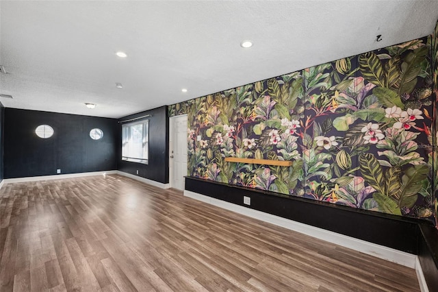 spare room featuring a textured ceiling, wallpapered walls, wood finished floors, and baseboards