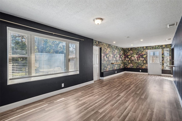 spare room with wallpapered walls, visible vents, baseboards, and wood finished floors