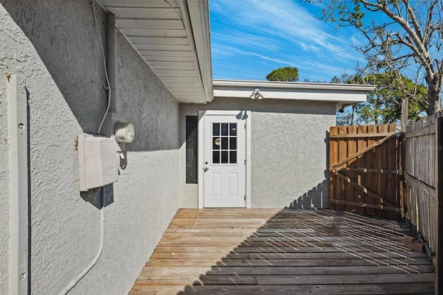 view of exterior entry featuring fence, a deck, and stucco siding