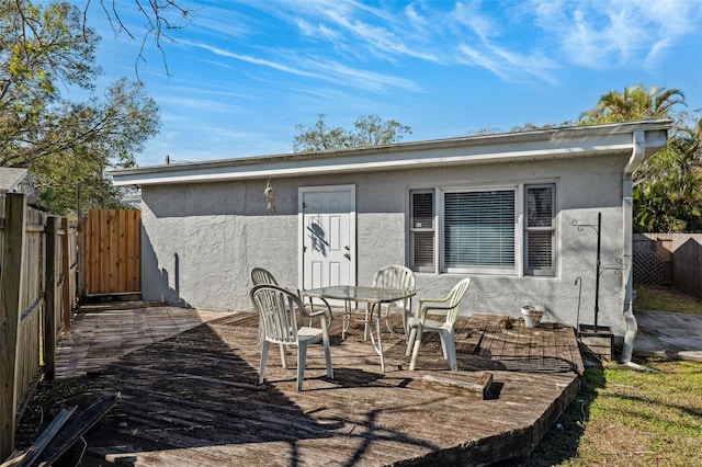 rear view of property with outdoor dining area, fence, a wooden deck, and stucco siding