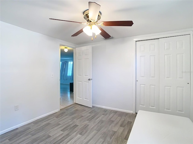 unfurnished bedroom with ceiling fan, light wood-type flooring, and a closet