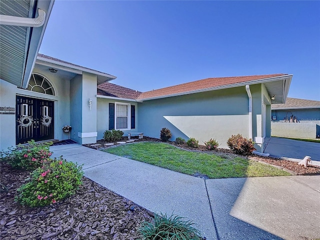 view of exterior entry featuring a lawn and stucco siding