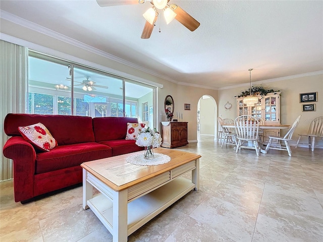 living room featuring arched walkways, ornamental molding, a ceiling fan, and baseboards