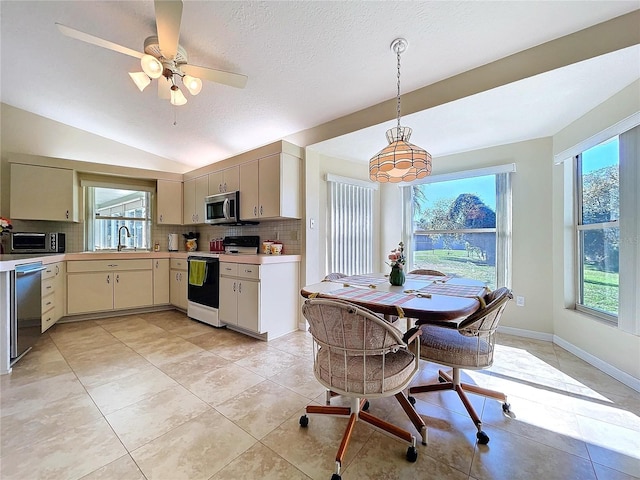 kitchen featuring cream cabinetry, stainless steel appliances, lofted ceiling, tasteful backsplash, and light countertops