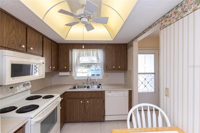 kitchen with sink, white appliances, ceiling fan, a tray ceiling, and light tile patterned flooring