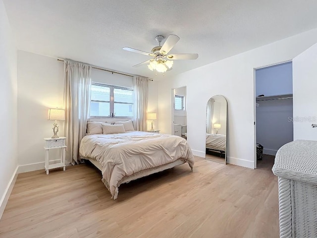 bedroom with a walk in closet, a textured ceiling, ceiling fan, and light hardwood / wood-style flooring