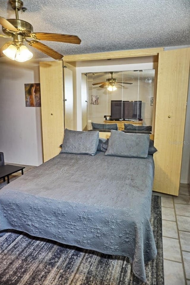 tiled bedroom with ceiling fan and a textured ceiling