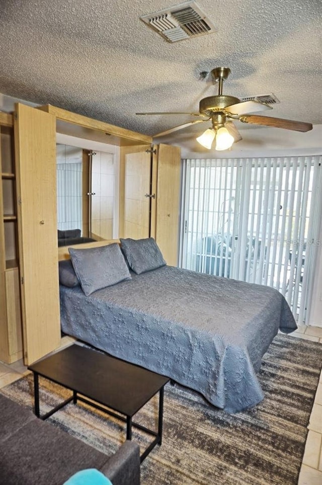 tiled bedroom with ceiling fan and a textured ceiling