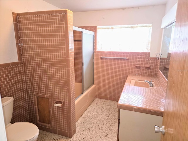 full bathroom featuring tile walls, vanity, enclosed tub / shower combo, and toilet