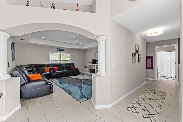 living room featuring ceiling fan, a tray ceiling, and decorative columns