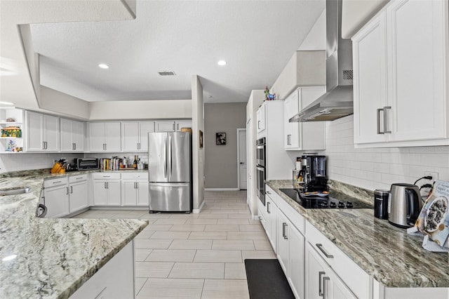 kitchen featuring appliances with stainless steel finishes, sink, white cabinets, light stone countertops, and wall chimney range hood