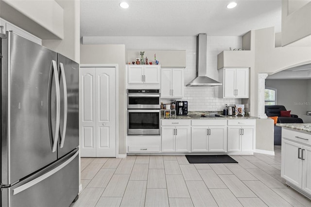 kitchen featuring white cabinetry, light stone countertops, appliances with stainless steel finishes, and wall chimney exhaust hood