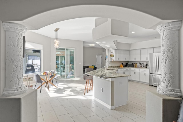 kitchen with white cabinetry, stainless steel fridge, hanging light fixtures, kitchen peninsula, and light stone countertops