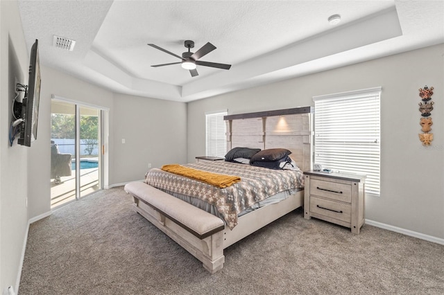 bedroom featuring a textured ceiling, light carpet, access to outside, a raised ceiling, and ceiling fan