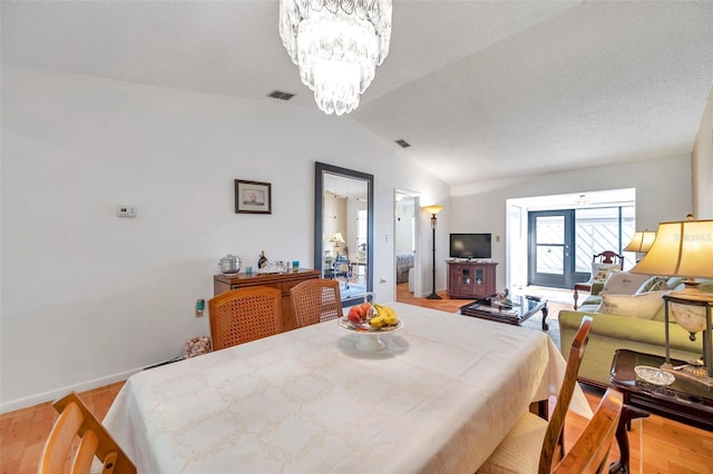 dining space featuring vaulted ceiling, a textured ceiling, a chandelier, and light hardwood / wood-style floors