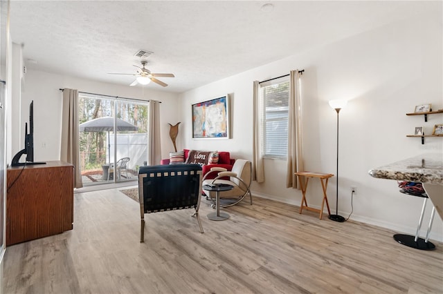 living room featuring ceiling fan, a textured ceiling, and light wood-type flooring