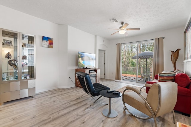 living room featuring ceiling fan, a textured ceiling, and light hardwood / wood-style floors