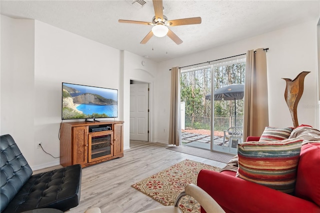 living room with ceiling fan, light hardwood / wood-style flooring, and a textured ceiling