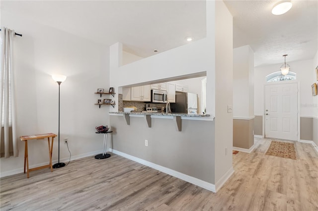 kitchen with light hardwood / wood-style flooring, stainless steel appliances, kitchen peninsula, and a breakfast bar