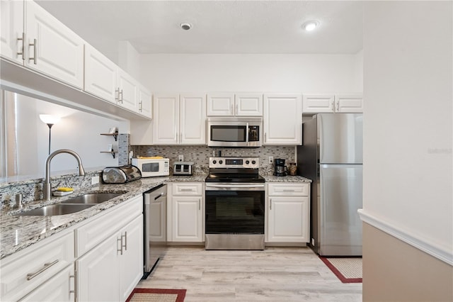 kitchen featuring sink, light stone counters, tasteful backsplash, stainless steel appliances, and white cabinets