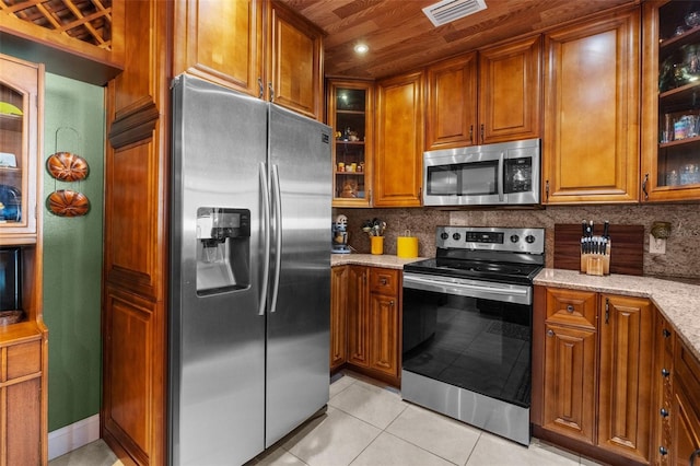 kitchen with light tile patterned flooring, appliances with stainless steel finishes, light stone counters, and decorative backsplash