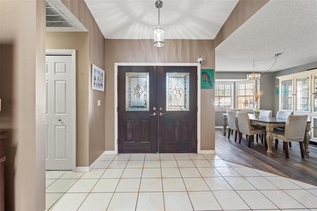 tiled foyer entrance with a textured ceiling, an inviting chandelier, and french doors