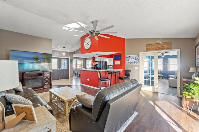 living room with wood-type flooring, vaulted ceiling with skylight, ceiling fan, and french doors