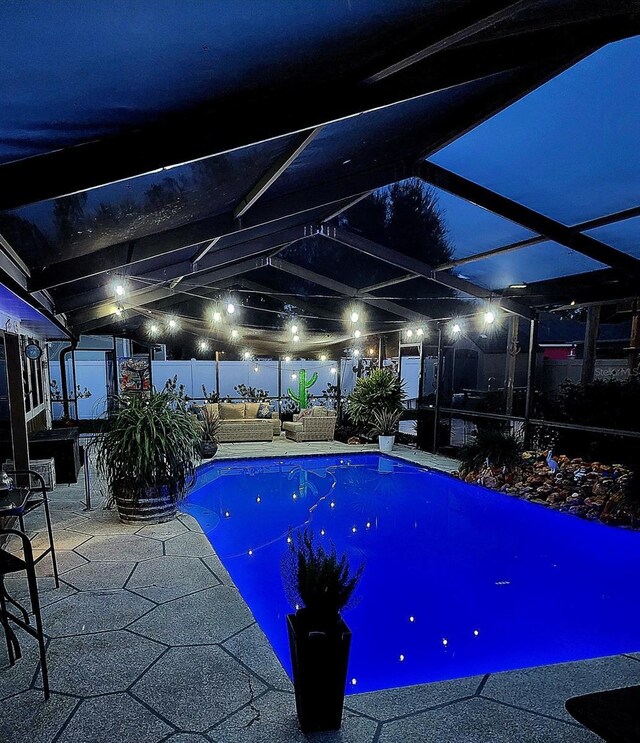 pool at night featuring a bar, outdoor lounge area, glass enclosure, and a patio area