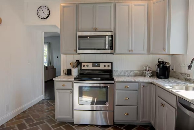 kitchen with stainless steel appliances, sink, gray cabinetry, and light stone counters