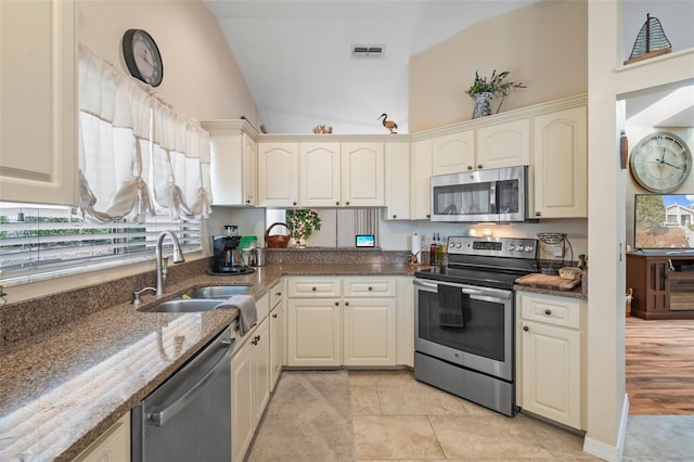 kitchen featuring lofted ceiling, sink, dark stone countertops, appliances with stainless steel finishes, and cream cabinets