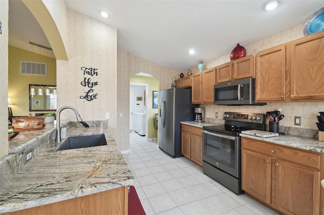 kitchen with sink, light tile patterned floors, appliances with stainless steel finishes, independent washer and dryer, and light stone countertops