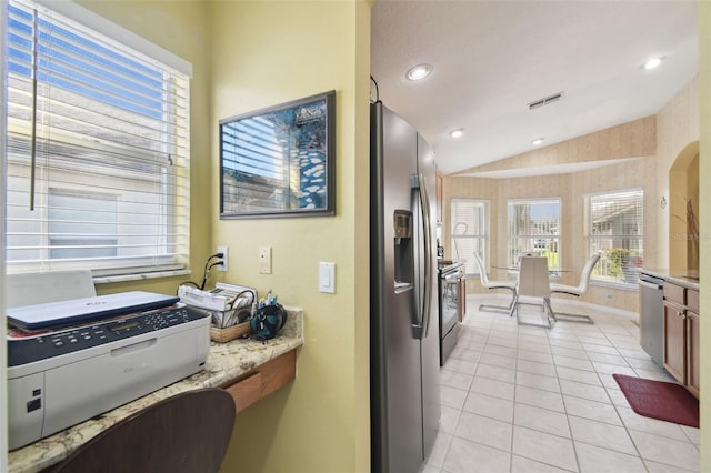 kitchen with light tile patterned flooring, appliances with stainless steel finishes, vaulted ceiling, and light stone counters