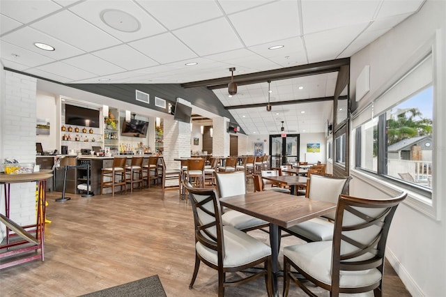 dining room featuring brick wall, a paneled ceiling, lofted ceiling, hardwood / wood-style flooring, and bar area