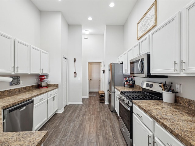 kitchen with white cabinetry, a towering ceiling, stainless steel appliances, and dark hardwood / wood-style floors