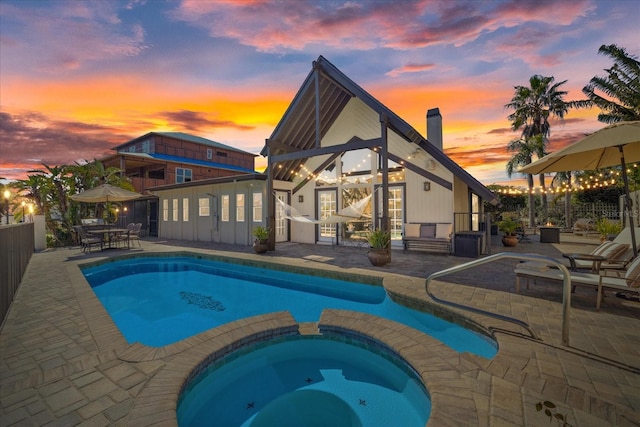 pool at dusk featuring a patio and an in ground hot tub