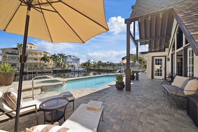 view of pool featuring an in ground hot tub, a water view, and a patio